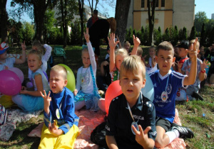 dzieci siedzą w ogrodzie i pokazują palce
